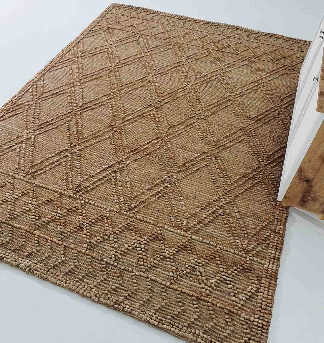 The RAMSHA HOME Floor Woven Living Room Rug SR-019 is a rectangular, natural-colored jute rug with diamond patterns and textured details in beige and brown, shown on a light floor beside wooden furniture.