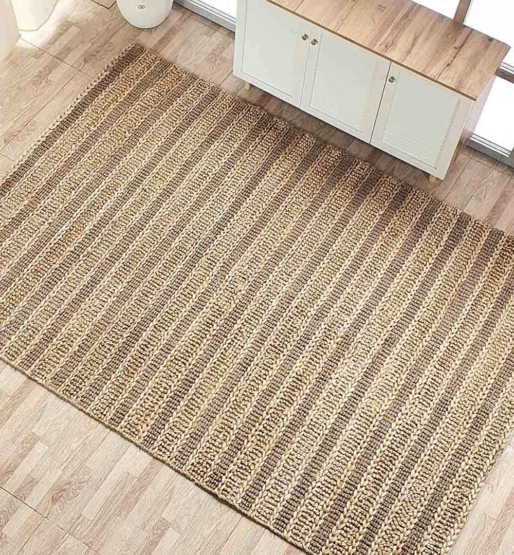 The RAMSHA HOME Jute Woven Home Decor Rug Natural Color SR-032, with a striped pattern, sits on a light wooden floor by a white cabinet and window, beautifully illuminated by natural light.