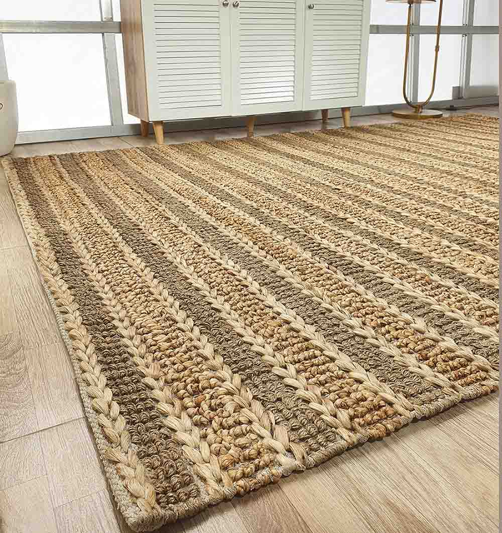 The RAMSHA HOME Jute Woven Home Decor Rug Natural Color SR-032, with alternating light and dark brown stripes, lies on a wooden floor by a white cabinet and large windows in a bright room.
