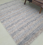 The RAMSHA HOME Wool Bedroom Rug, Living room Rug SR-050, a modern flatweave with chunky knit stripes in beige, gray, and white, lies on a light floor beside a wooden table leg.