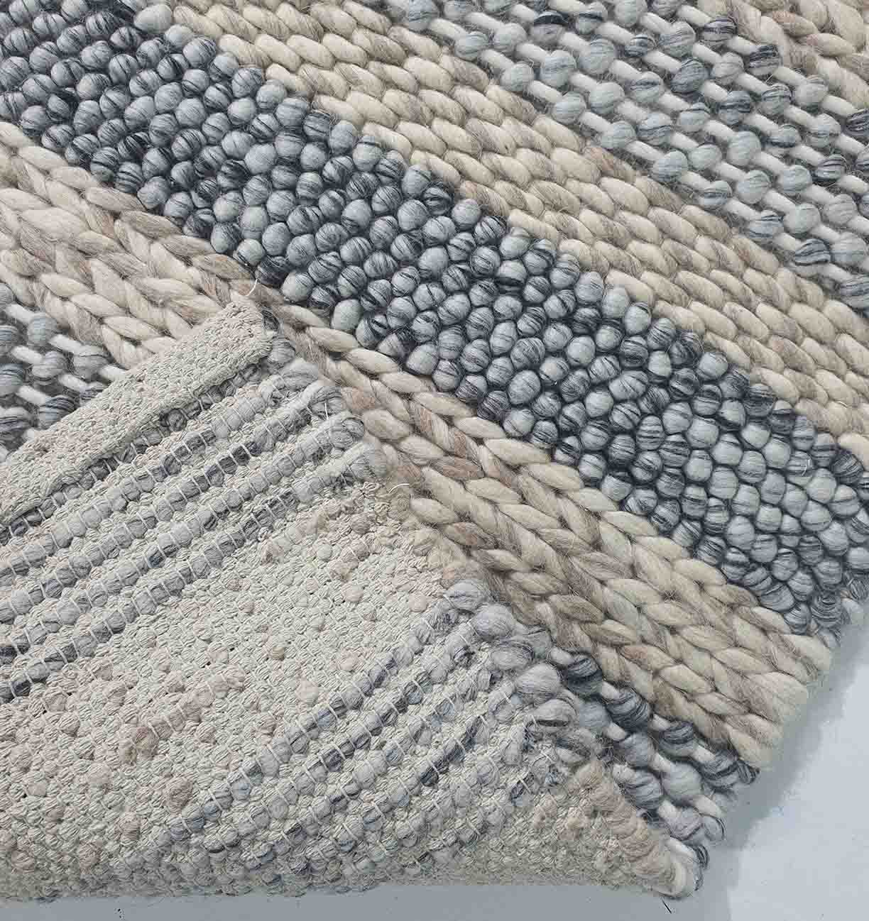 A close-up of the RAMSHA HOME Wool Bedroom Rug SR-050 shows chunky cream, gray, and beige yarn. A folded corner reveals a lighter striped underside—ideal for those who love the look of a striped woven rug in any space.