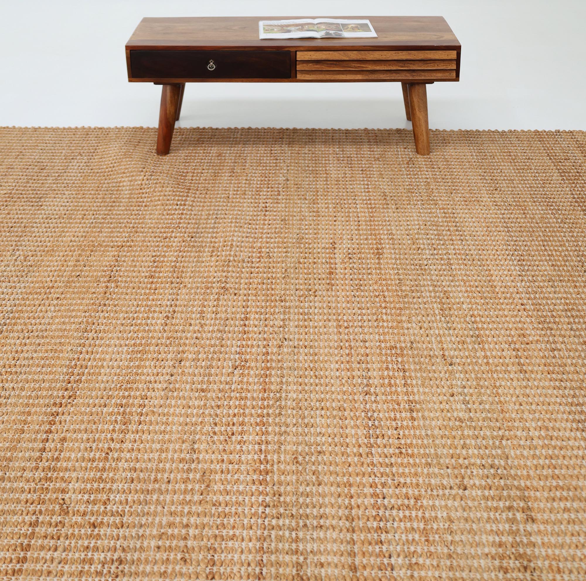The RAMSHA HOME Handmade Natural Color Hand Woven Area Rug SR-062 lies on the floor, paired with a mid-century modern wooden coffee table holding a magazine, all set against a plain white background.