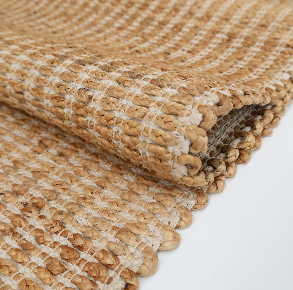 A close-up of the RAMSHA HOME Handmade Natural Color Hand Woven Area Rug SR-062 displays its thick textured weave in tan and beige tones, with a folded corner on a white surface—an elegant piece for artisanal home décor.