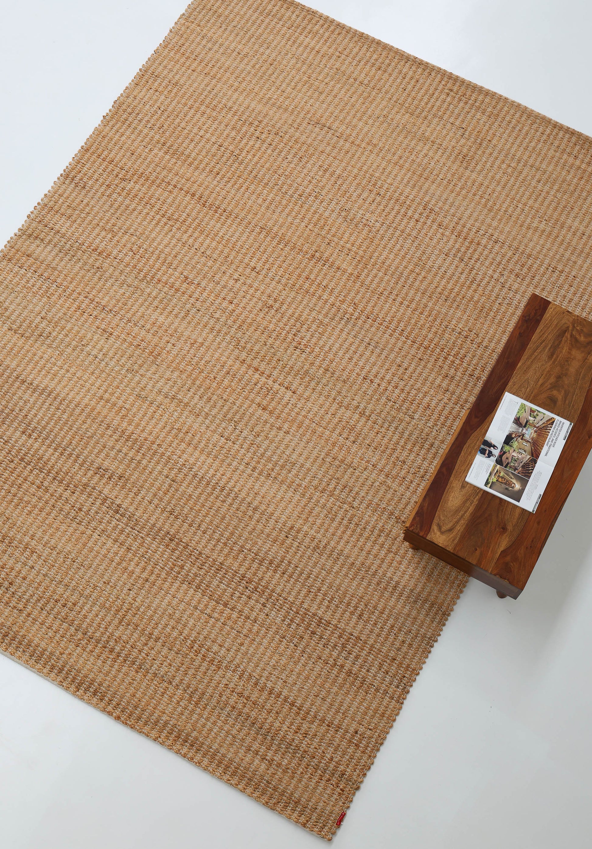 The RAMSHA HOME Handmade Natural Color Hand Woven Area Rug SR-062 anchors the white floor, while a wooden bench with a magazine in the upper right corner adds artisanal charm to the décor.