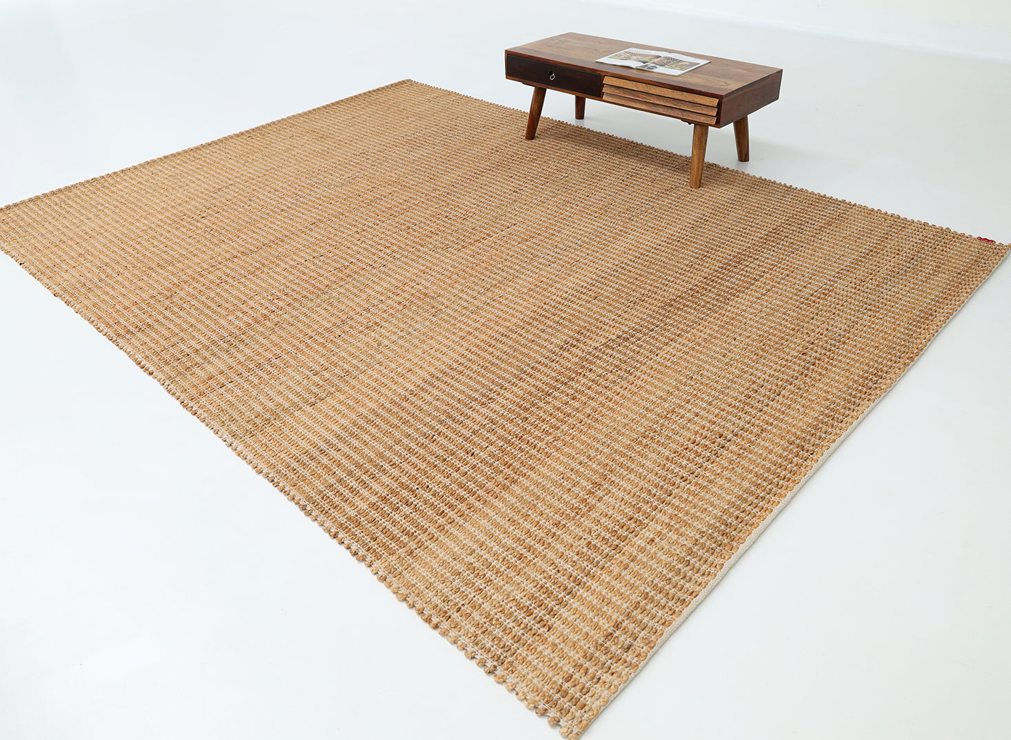 The RAMSHA HOME Handmade Natural Color Hand Woven Area Rug SR-062 adds artisanal charm to your space, resting on a white floor with a small wooden coffee table holding magazines in the corner.