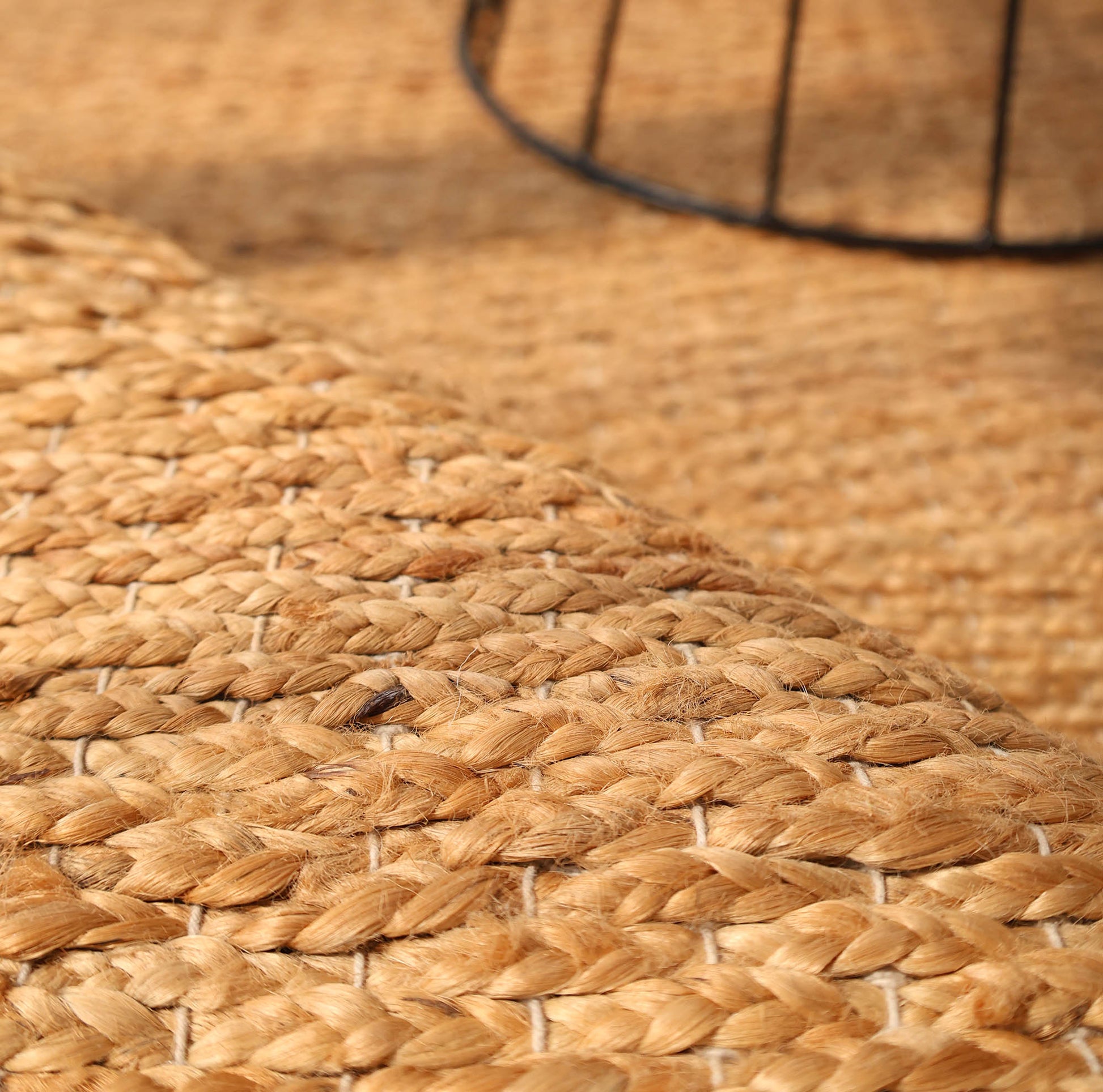 Close-up of the RAMSHA HOME Handmade Natural Color Hand Woven Area Rug SR-063, featuring a braided texture. A black metal furniture leg casts a shadow on this artisanal home décor piece.