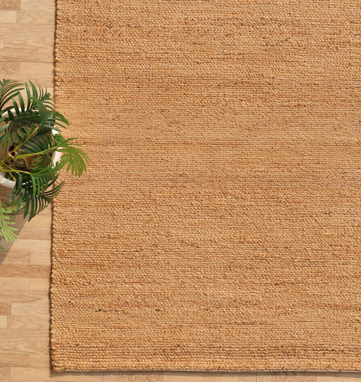 The Handmade Natural Color Hand Woven Area Rug SR-064 by RAMSHA HOME rests elegantly on a light wood floor, while a green potted plant partially placed in the bottom left corner adds an inviting touch—an artisanal accent that brings warmth and style to any space.