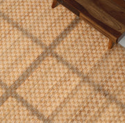 A close-up of the RAMSHA HOME Handmade Natural Color Hand Woven Area Rug SR-065, featuring a textured beige and light brown checkered pattern, partially placed beneath wooden furniture with angled legs.