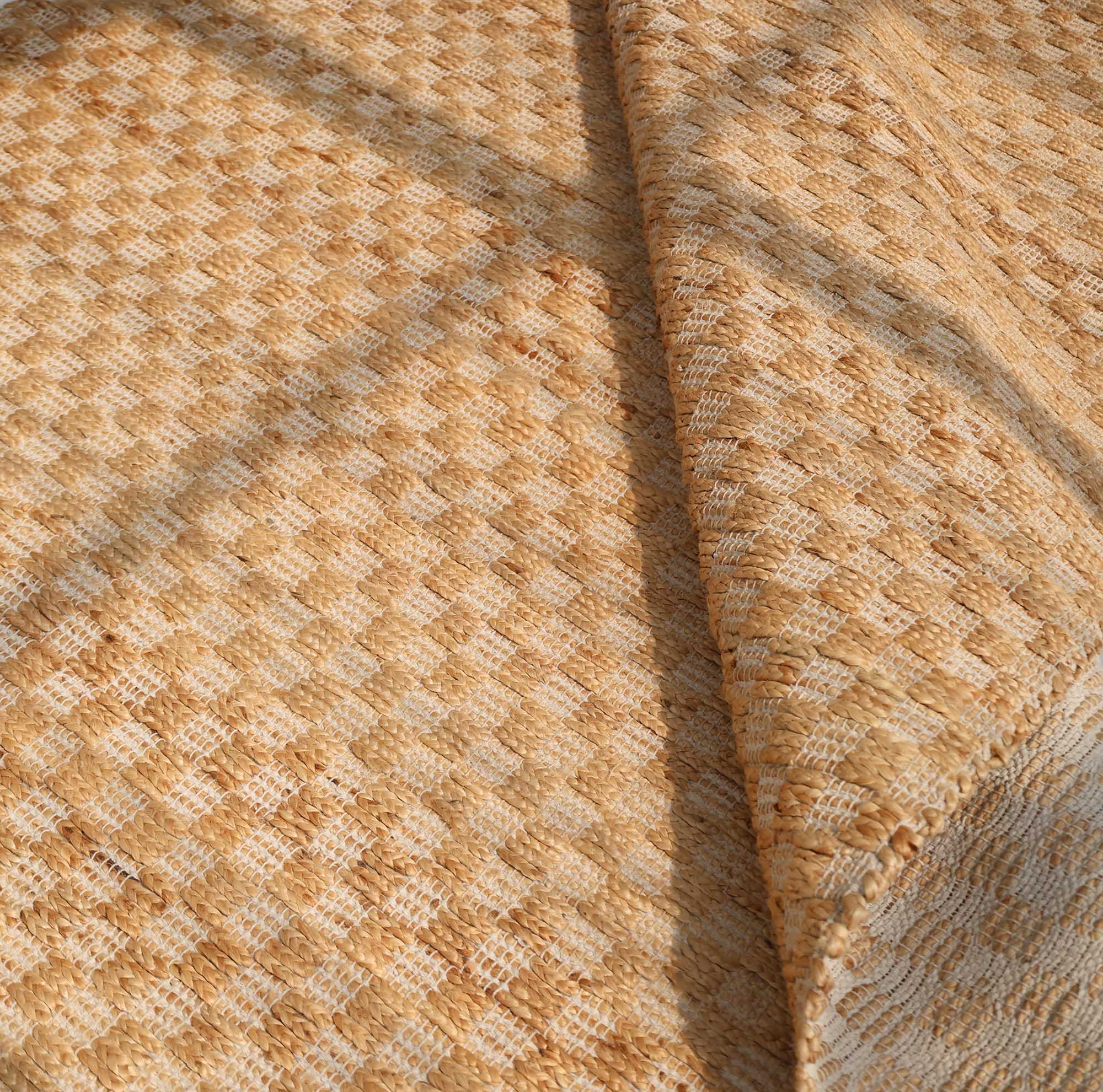 The RAMSHA HOME Handmade Natural Color Hand Woven Area Rug SR-065 features a beige woven checkered texture, shown partially folded with soft sunlight—ideal for artisanal home décor or inspiring your own handmade creations.