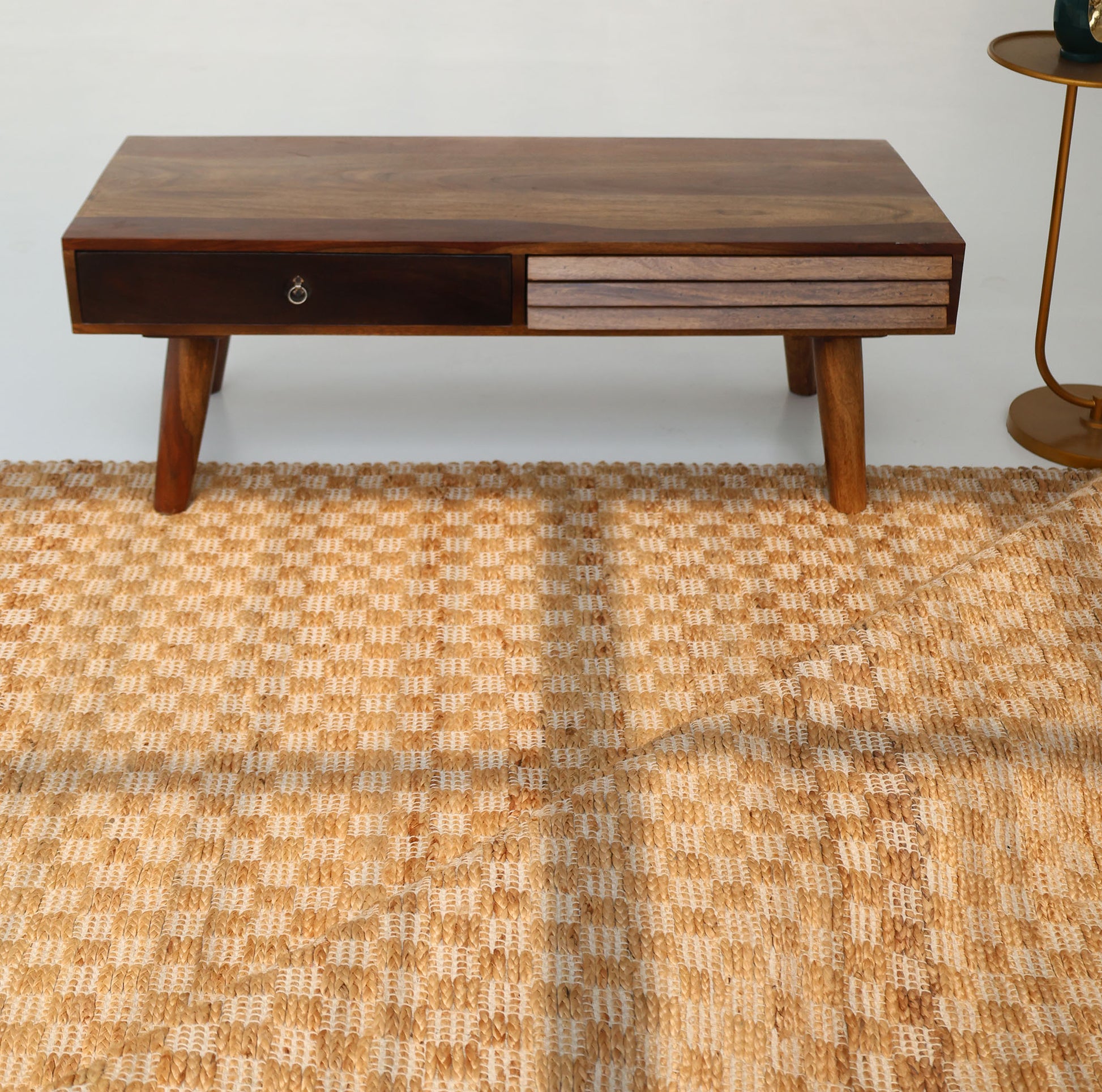 A wooden coffee table with angled legs, a drawer, and a two-tone front stands on the RAMSHA HOME Handmade Natural Color Hand Woven Area Rug SR-065. A small round side table with a green cup is partially visible to the right.