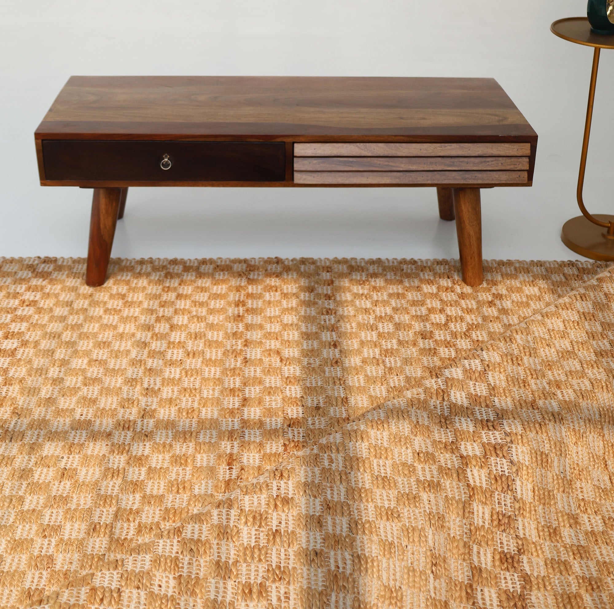 A wooden coffee table with angled legs, a drawer, and a two-tone front stands on the RAMSHA HOME Handmade Natural Color Hand Woven Area Rug SR-065. A small round side table with a green cup is partially visible to the right.