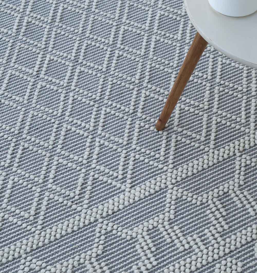 The RAMSHA HOME Wool & Cotton Woven Rug Area Rug SRN-004, in gray and white with a geometric diamond pattern, is shown close-up beside a round table with wooden legs.