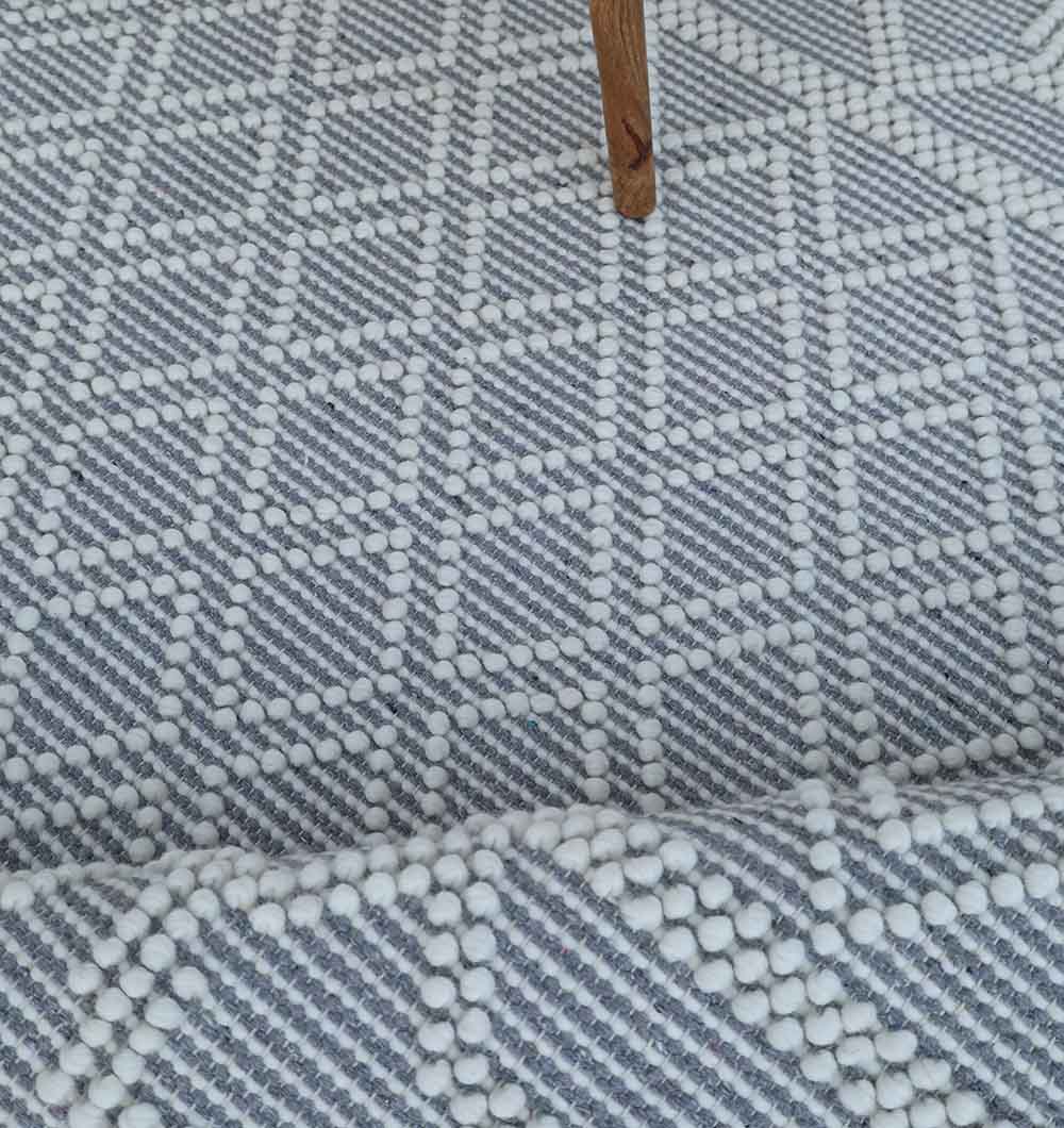 A close-up of the RAMSHA HOME Wool & Cotton Woven Rug Area Rug SRN-004 on stairs, featuring a modern geometric pattern in white and light gray, with a wooden furniture leg in the background.