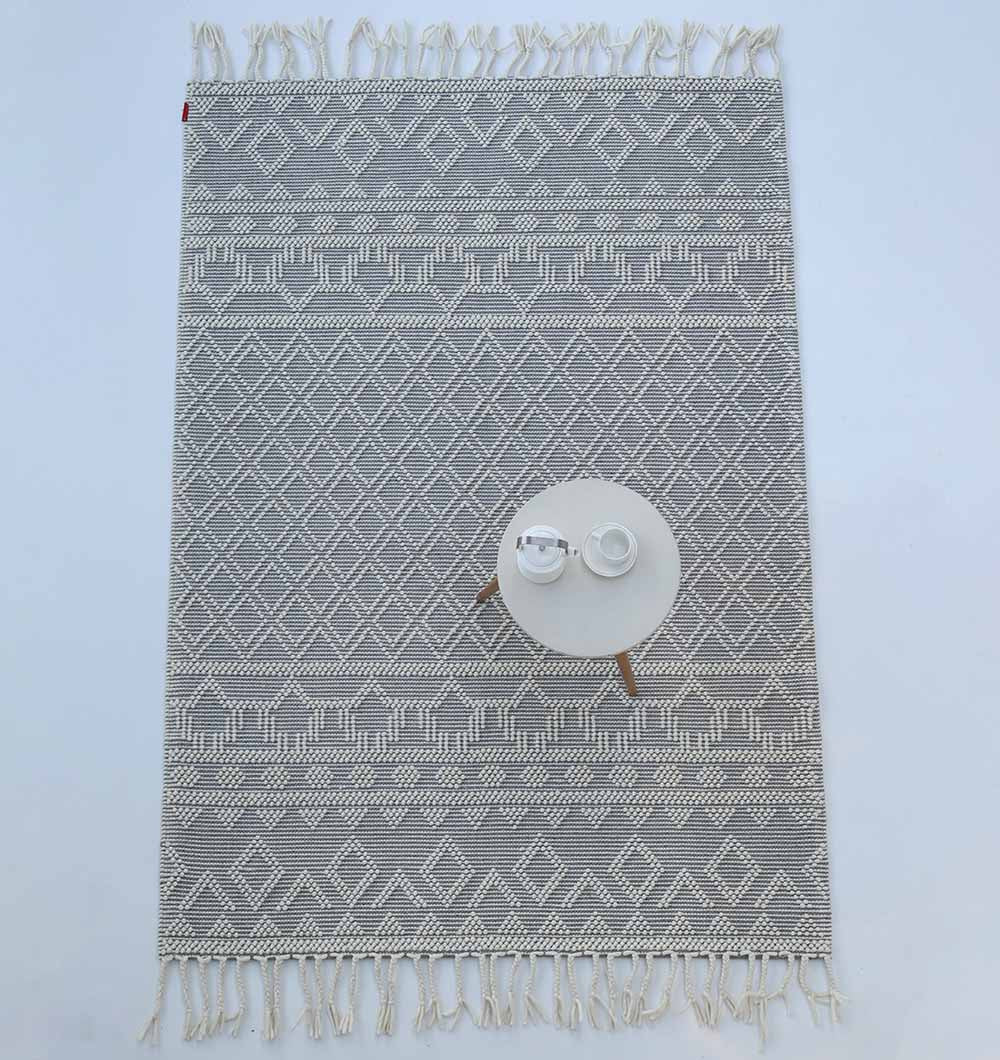 The RAMSHA HOME Wool & Cotton Woven Rug Area Rug SRN-004, featuring a gray and white pattern with fringe edges, is shown from above with a small round white table, teapot, and two teacups on its lower right corner.
