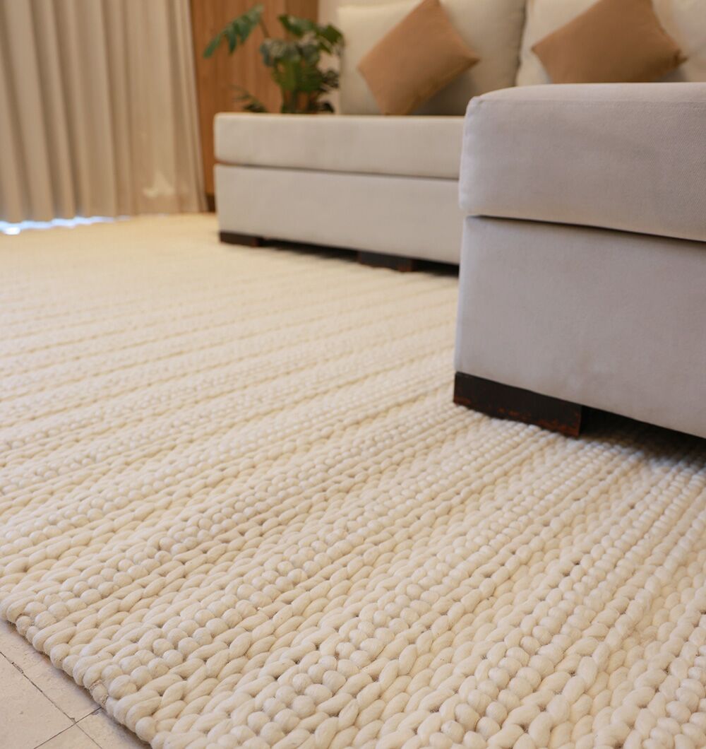 Close-up of the Eid Festive Collection Natural White Rectangle Rug SRN 008—its textured cream design is an ideal Ramadan décor accent—shown with a light beige sofa, brown pillows, potted plant, and curtains in the living room.