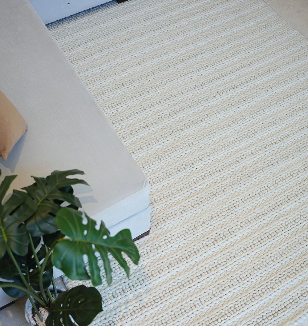 The Eid Festive Collection Natural White Rectangle Rug SRN 008 is placed beside a light gray sofa, while a large-leaf green potted plant in the corner creates a serene atmosphere, perfect for Eid home décor.