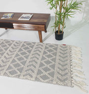 The RAMSHA HOME Ramadan Prayer Rugs Natural White Floor Woven Rug with Fringes SRN 020 lies on a white floor beside a wooden coffee table with magazines and a potted green plant in the background.