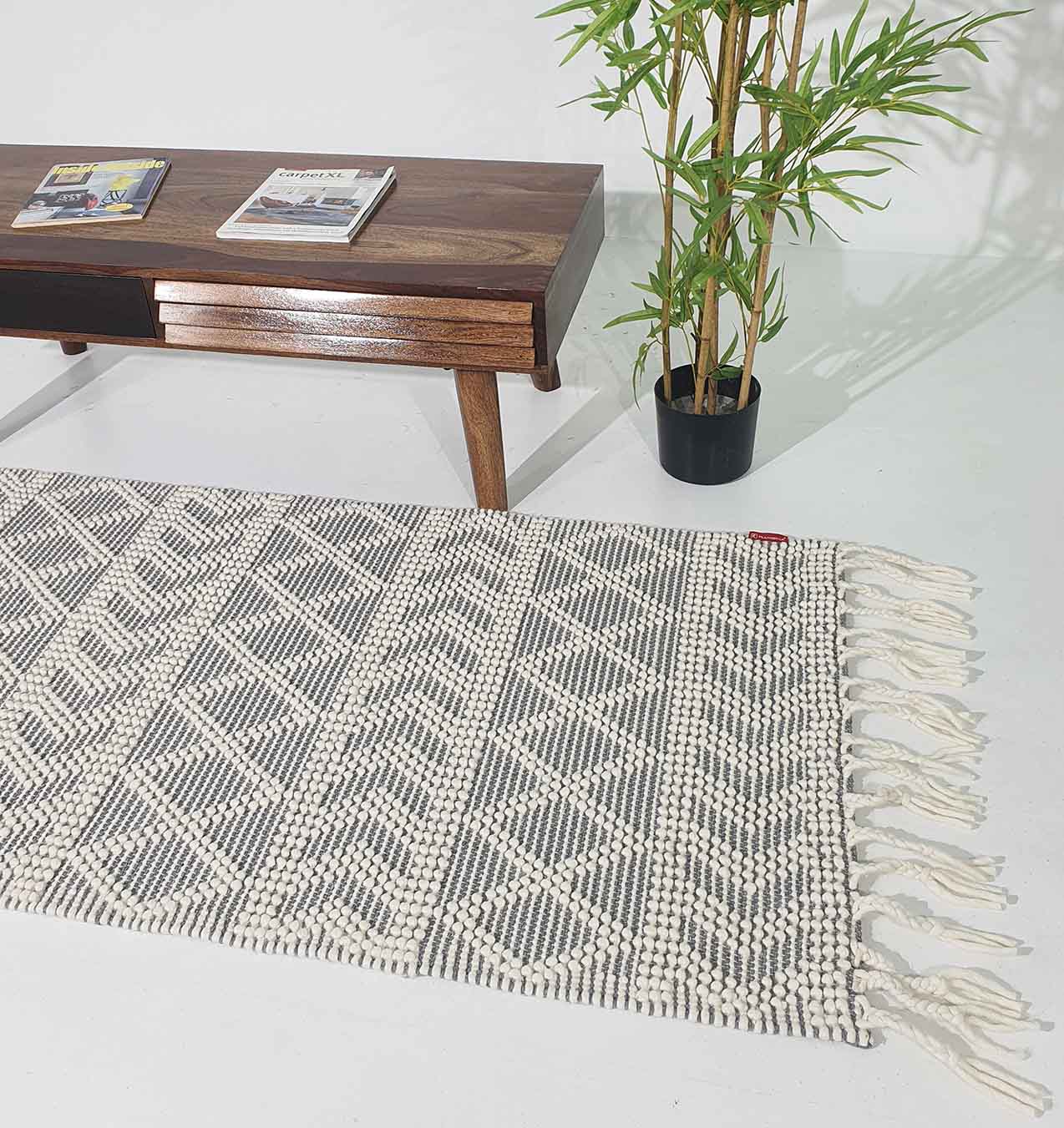 The RAMSHA HOME Ramadan Prayer Rugs Natural White Floor Woven Rug with Fringes SRN 020 lies on a white floor beside a wooden coffee table with magazines and a potted green plant in the background.