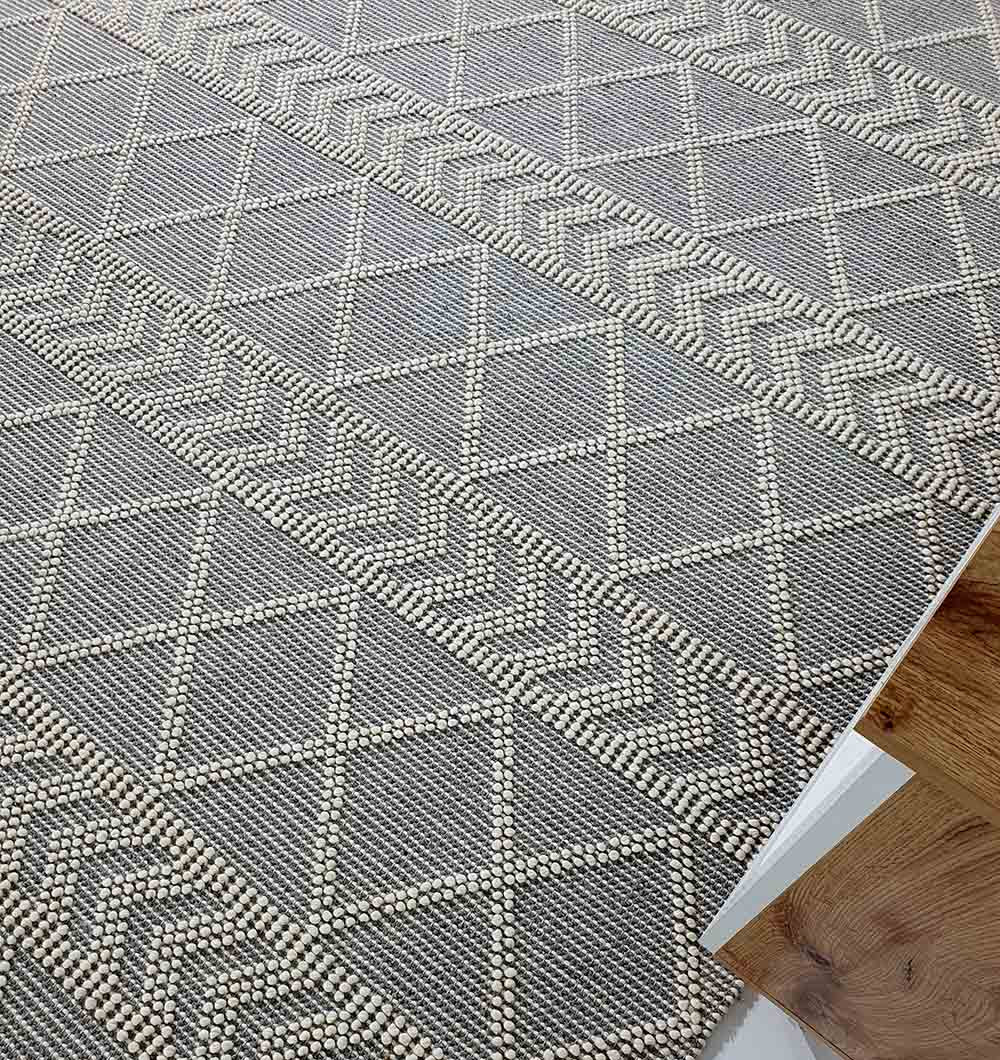 Close-up of the RAMSHA HOME Ramadan Prayer Rugs Natural White Floor Woven Rug with Fringes SRN 020, featuring a textured geometric pattern, bordered by a wooden floor in the lower right corner.