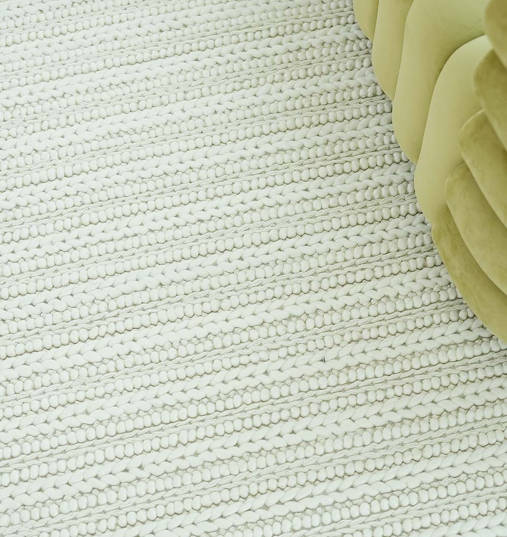 The RAMSHA HOME Natural White Woven Rug For Home Decore SRN-028, featuring textured raised and flat rows, is displayed beside a light green, wavy upholstered sofa.