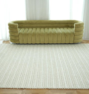 A modern living room featuring a curved olive green velvet sofa and the RAMSHA HOME Natural White Woven Rug For Home Decore SRN-028 on a wooden floor, complemented by sheer white curtains in the background.