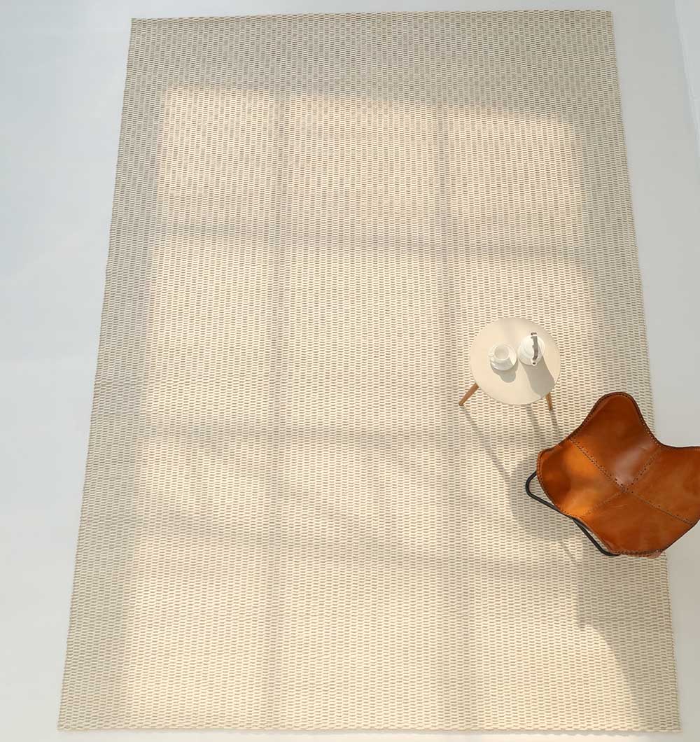 Sunlight streams onto the RAMSHA HOME Handmade Natural White Woven Rug For Home Decor SRN-030, casting grid-like shadows. In the corner, a brown leather chair and a small round table with a white teapot and cup complete the scene.