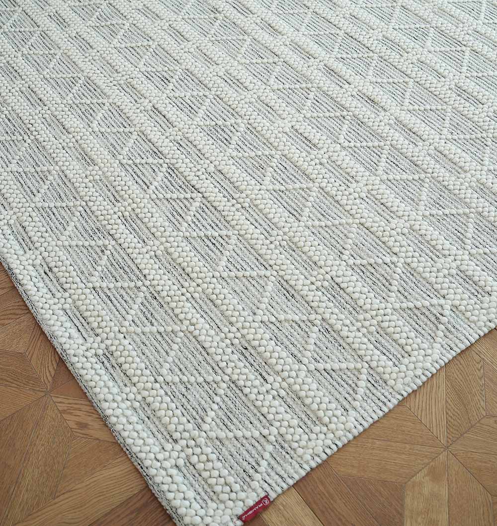 A close-up of the RAMSHA HOME Wool Woven Rug Area Rug with Natural Color SRN-040 in a geometric diamond pattern is shown on a wooden parquet floor, featuring a small red tag on the corner.
