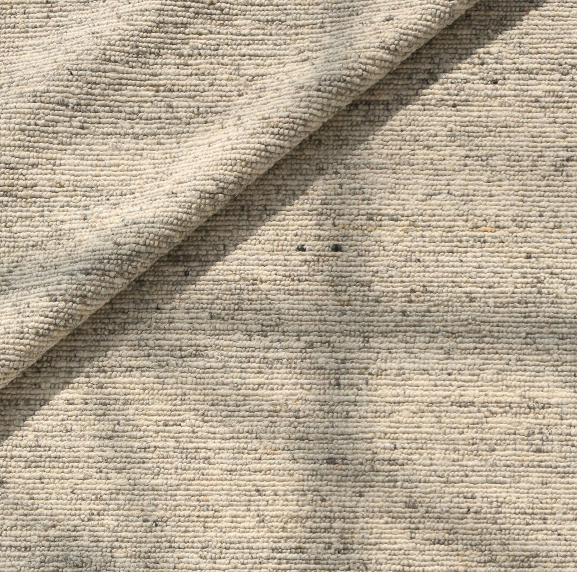 A close-up of the Soft Terra Flatweave Wool Rug (SRN-043) by RAMSHA HOME shows its beige organic texture and visible fibers, softly folded at the center to create gentle shadows—a nod to traditional craftsmanship.