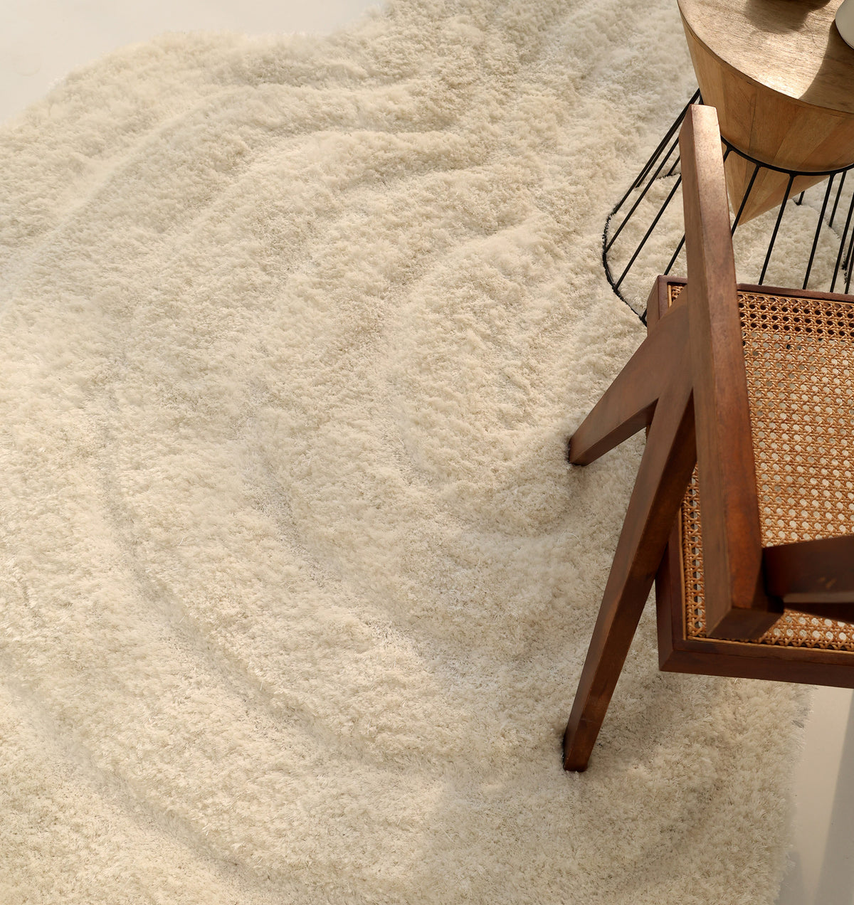 A white, irregular-shaped shaggy rug from RAMSHA HOME (SG 040 3D) is displayed next to a wooden chair with a woven seat and a small round side table.