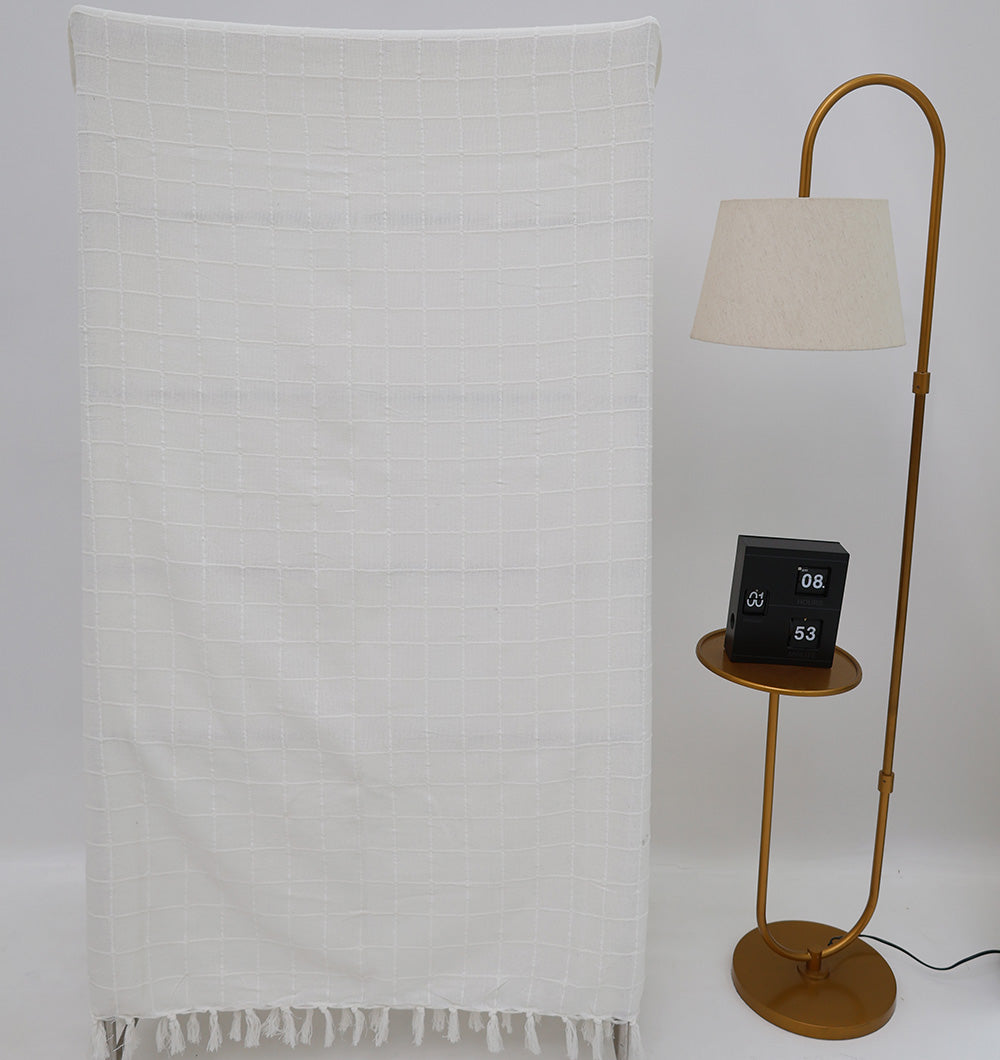 The White Decor Throw TAL 051 (130x160cm) by Ramsha Home hangs beside a gold floor lamp with a beige shade and a round table with a black digital clock, creating modern comfort against a plain white background.
