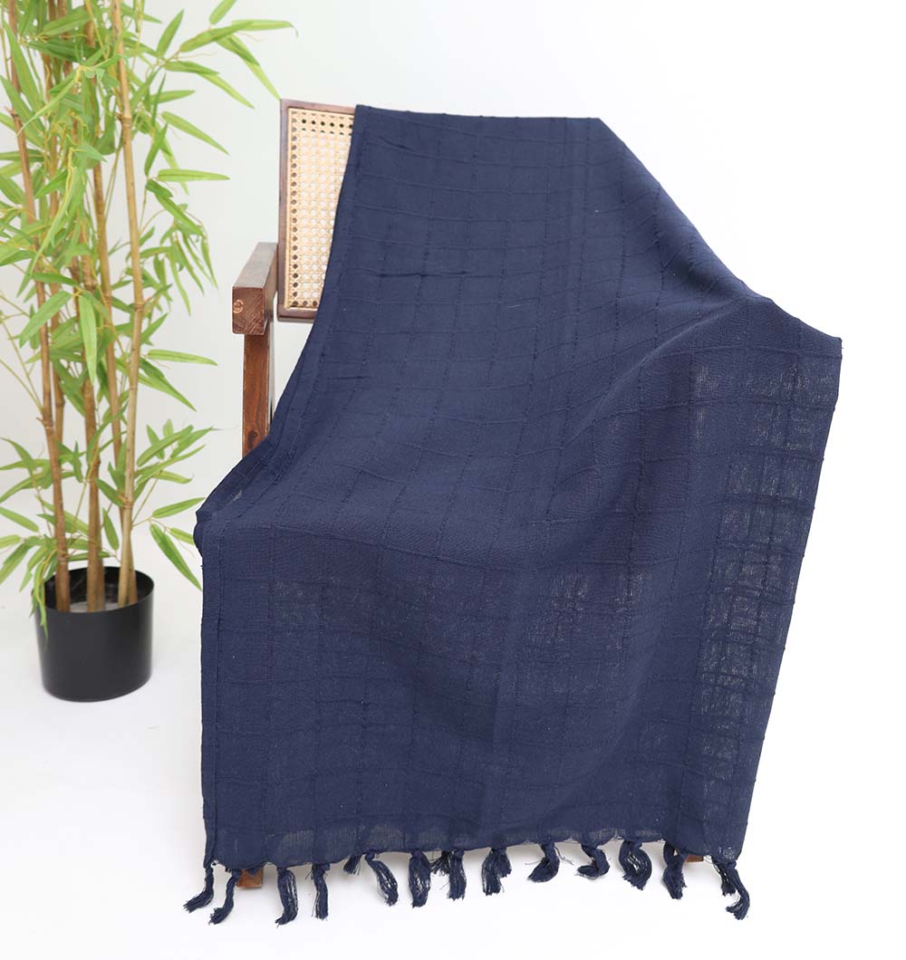The Living Room Throw Navy Blue Color TAL 055 (130x160cm) by Ramsha Home adds rich texture and style to any space, draped over a wooden chair beside a potted bamboo plant—perfect for a luxurious accent.