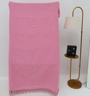 The Living Room Throw Pink Color TAL 056 (130x160cm) by Ramsha Home adds a touch of luxury to your decor, draped elegantly beside a gold floor lamp with side table and clock. The scene is set against a plain white background.