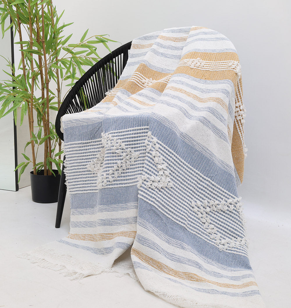 A black chair features the Ramsha Home Living Room Throw Multi Color Cotton Throws TAL 059 (130x150 cm), showcasing blue, white, and tan stripes with diamond patterns; a potted green plant sits nearby against a plain white background.