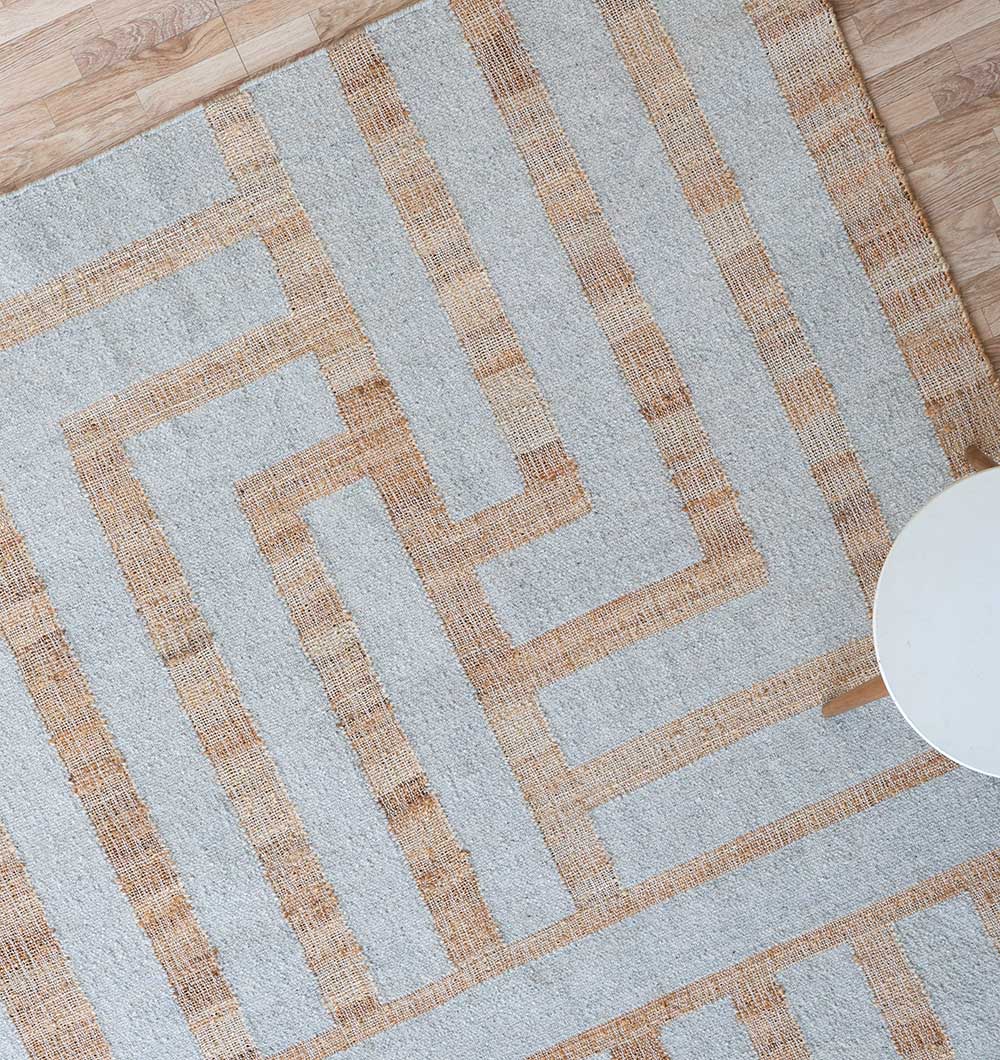 The RAMSHA HOME Jute & Wool Natural Color Hand Woven Rug WR-036, featuring a modern maze design in beige and light brown on gray, is flat woven for durability and placed on a wooden floor with a small round white table in the corner.