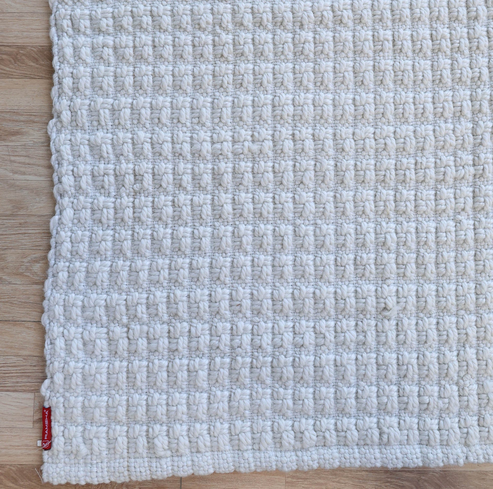 A close-up of the RAMSHA HOME Handmade Cream Natural Color Hand Woven Area Rug WR-039 displayed on a light wooden floor, featuring its textured surface and a small red tag near the bottom left corner.