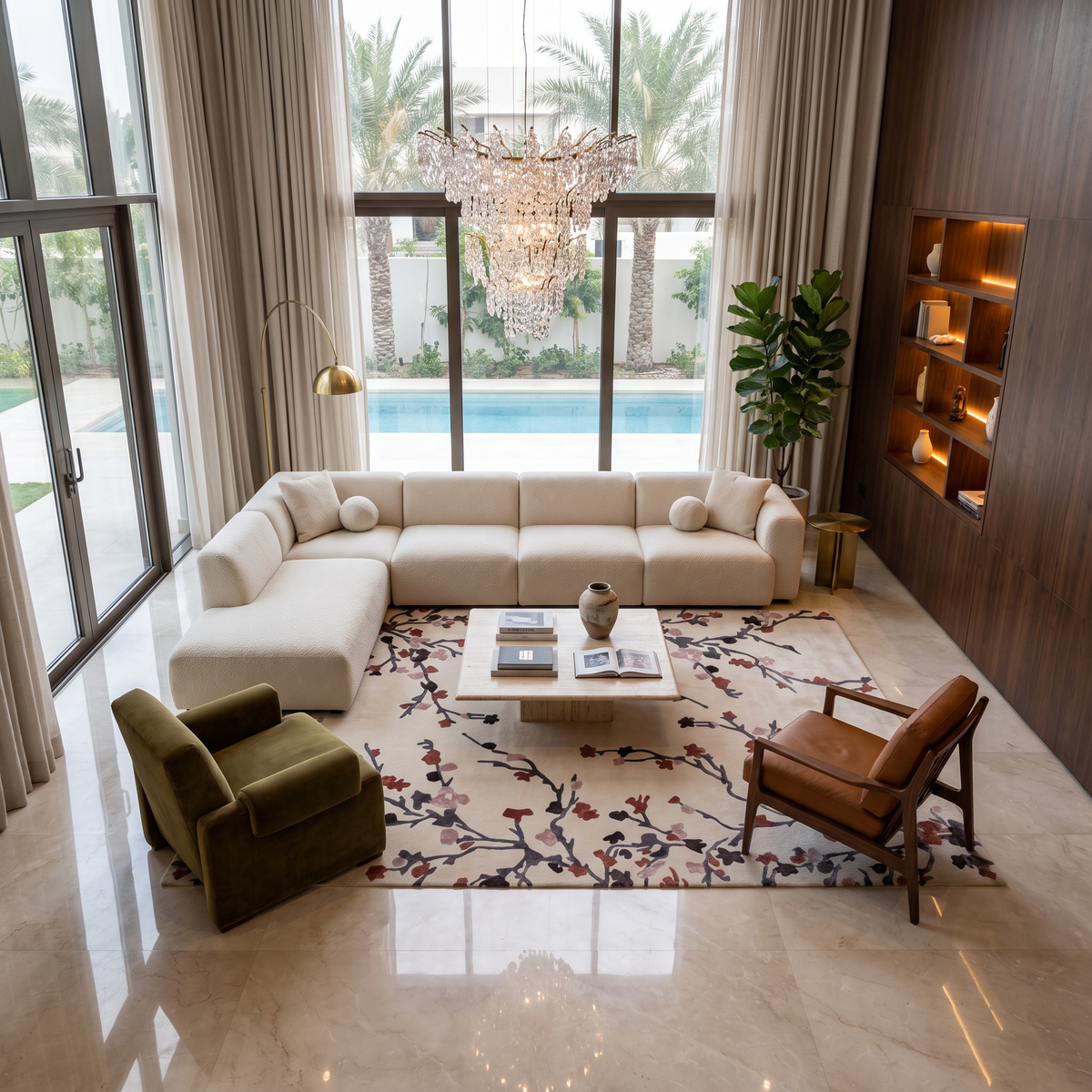 Modern living room featuring a large white sectional sofa, two armchairs, and a coffee table set atop the Multi Color Handmade Area Rug HTWV-119 by RAMSHA HOME. Tall windows fill the space with sunlight, accentuating the elegant chandelier, built-in shelves, and offering a stunning view of the pool with palm trees outside.