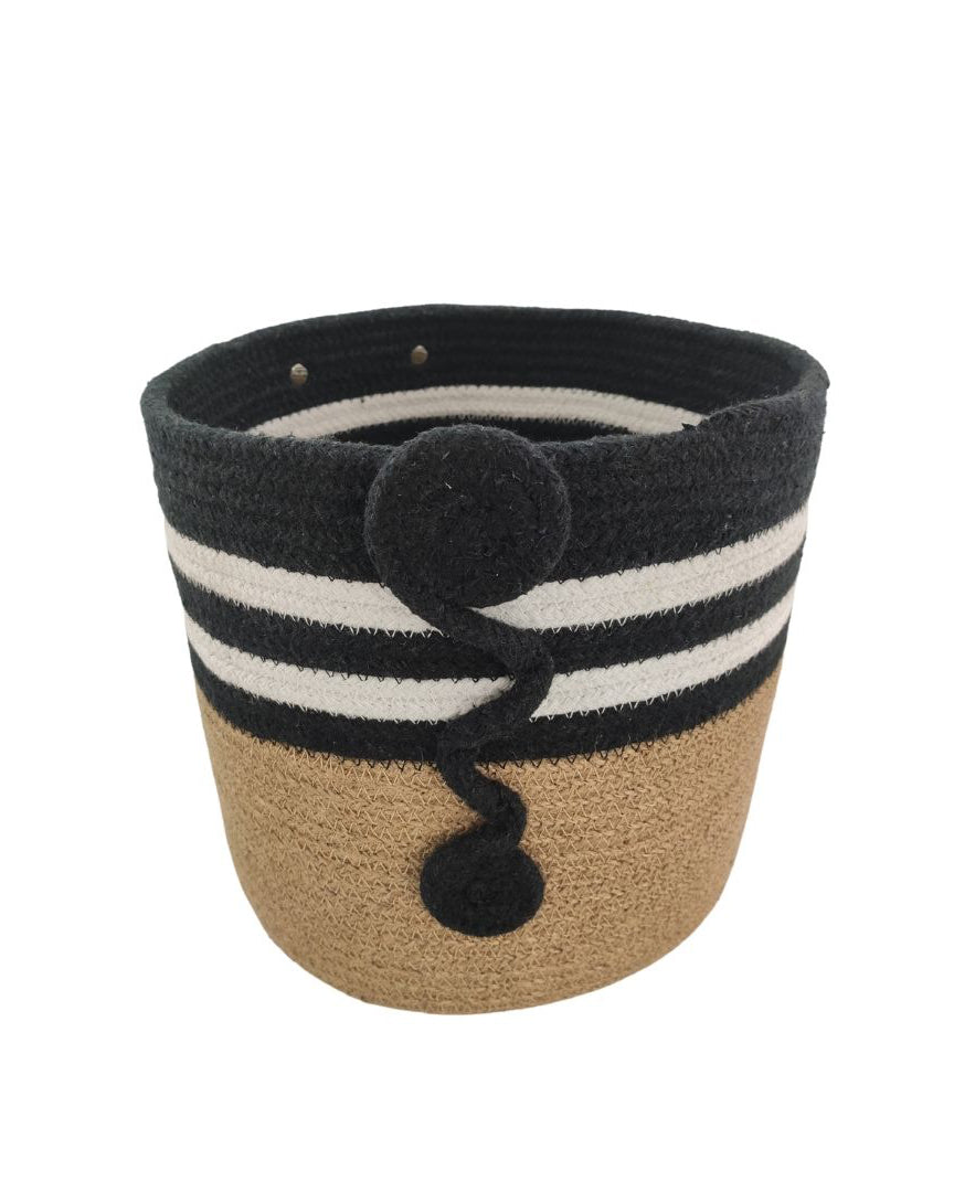 The Jute & Cotton Natural Handmade Basket - BS 004 (25x25cm) from Ramsha Home features a tan base, black upper half, two white stripes, and spiral black rope design—ideal for stylish toy storage or adding charm to your nursery decor.