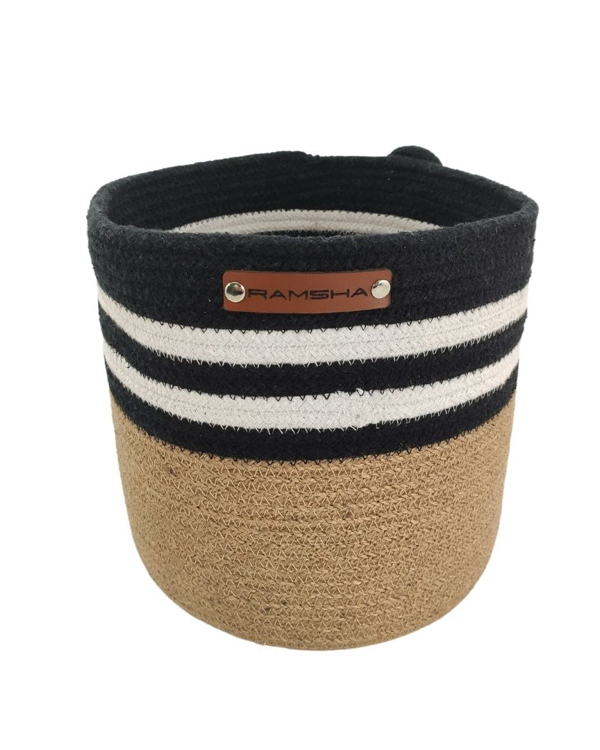 The Ramsha Home Jute & Cotton Natural Handmade Basket - BS 004 (25x25cm) features a tan base, black upper half with two white stripes, and a brown label—ideal for toy storage or as stylish nursery decor.