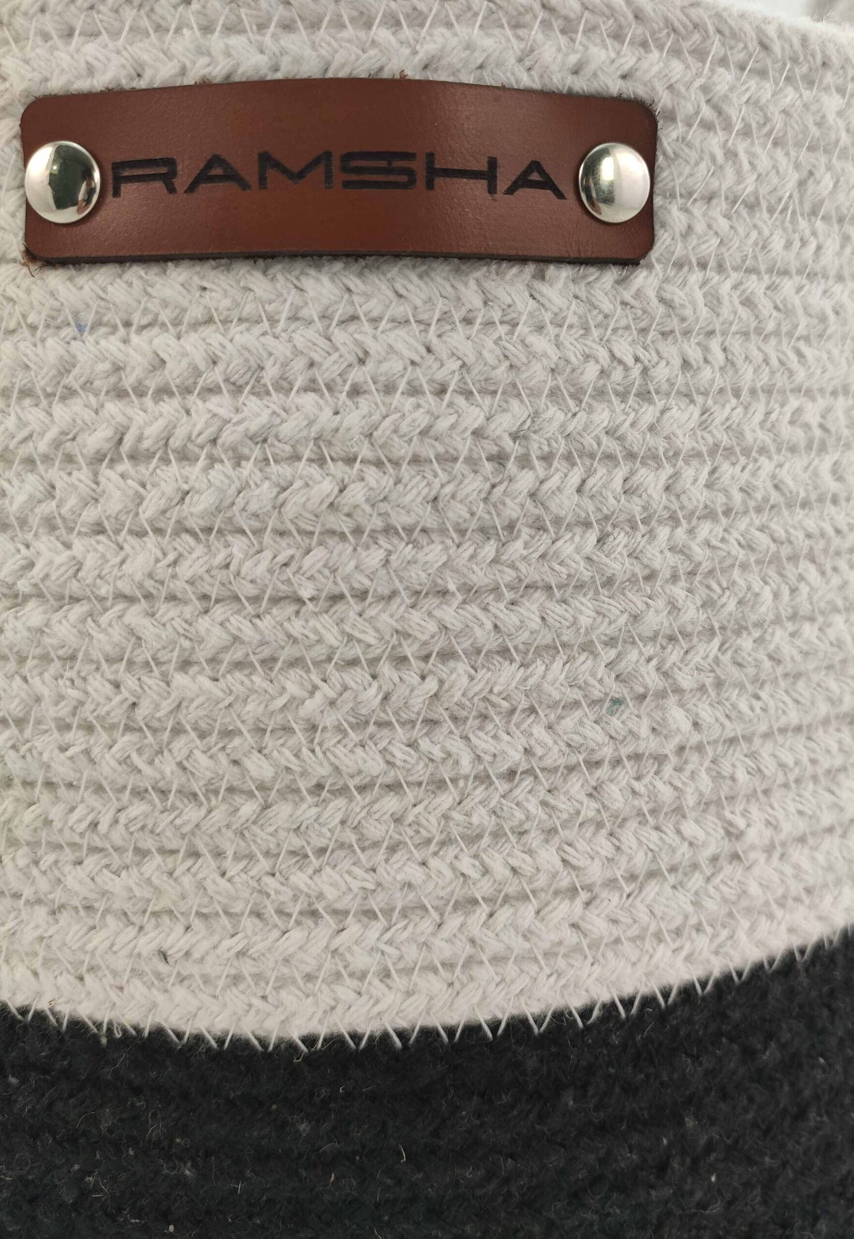 A close-up of the Ramsha Home Cotton White & Black Handmade Basket (25x25cm), with a brown leather RAMSHA label secured by metal rivets. This stylish basket is perfect for toy storage and chic nursery decor.