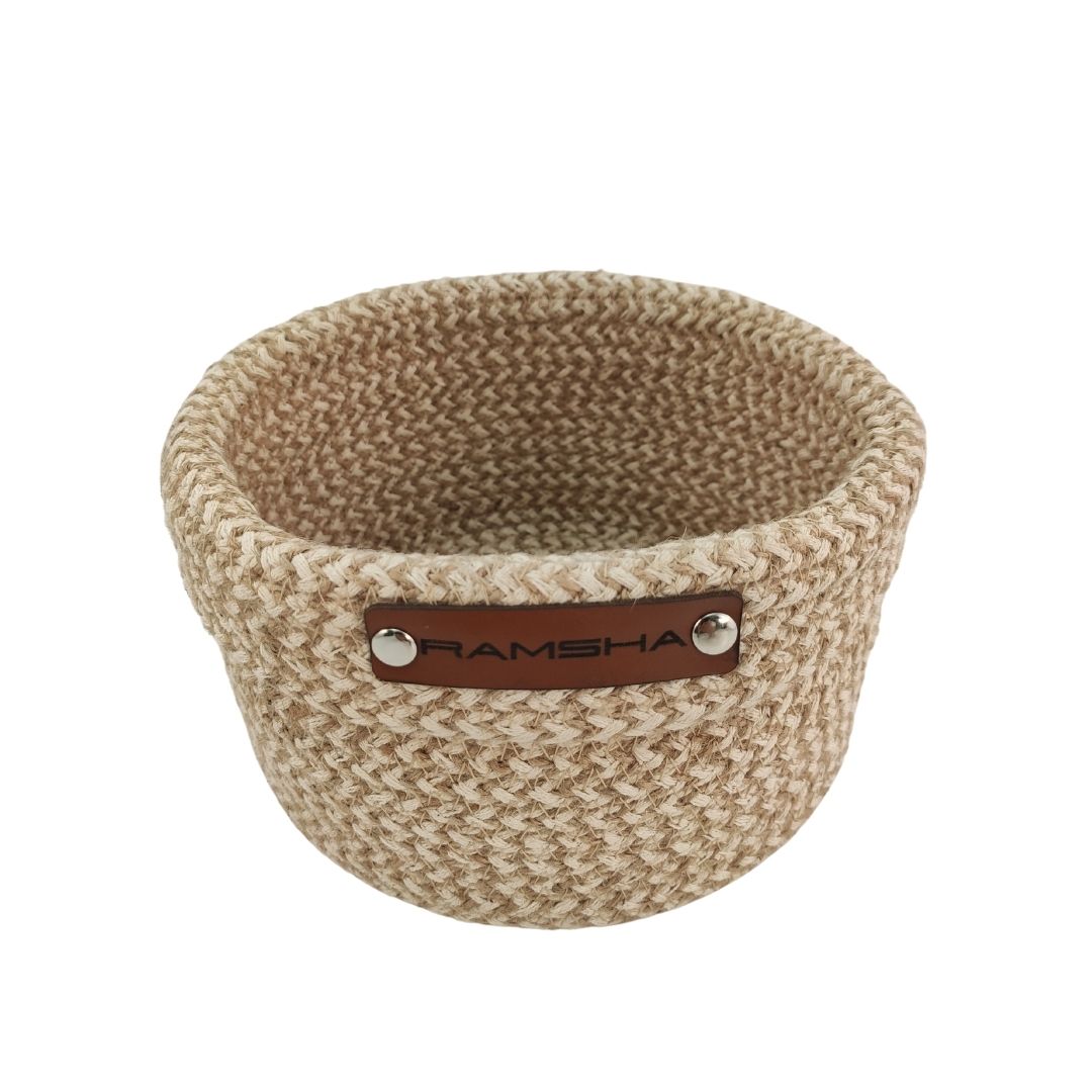 The Natural and White Handmade Jute and Cotton Basket (BS 008, 12x20 cm) by Ramsha Home features a textured pattern, brown leather label with RAMSHA embossed, perfect as a stylish home organizer or decor against a white background.