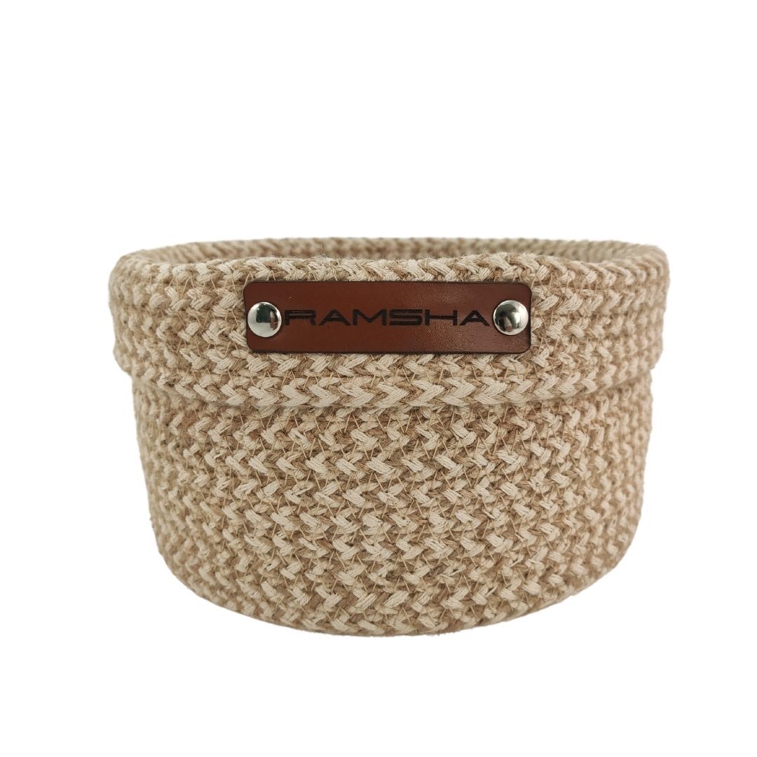 The Natural and White Handmade Jute and Cotton Basket for Home - BS 008 (12x20 cm) by Ramsha Home features a woven design, a front brown leather "RAMSHA" label, and is ideal as a stylish organizer or decor accent.