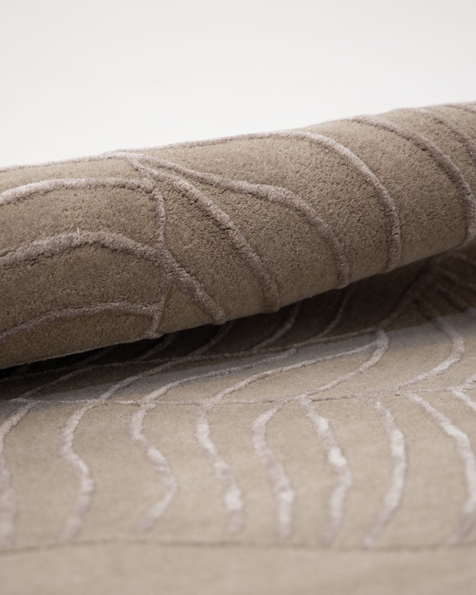 A close-up of the RAMSHA HOME Natural White Color Handmade Area Rug (HTWV-137, 200x300 cm) showcases its modern design in beige, with raised, wavy line patterns reminiscent of abstract area rugs, partially rolled over on a white background.