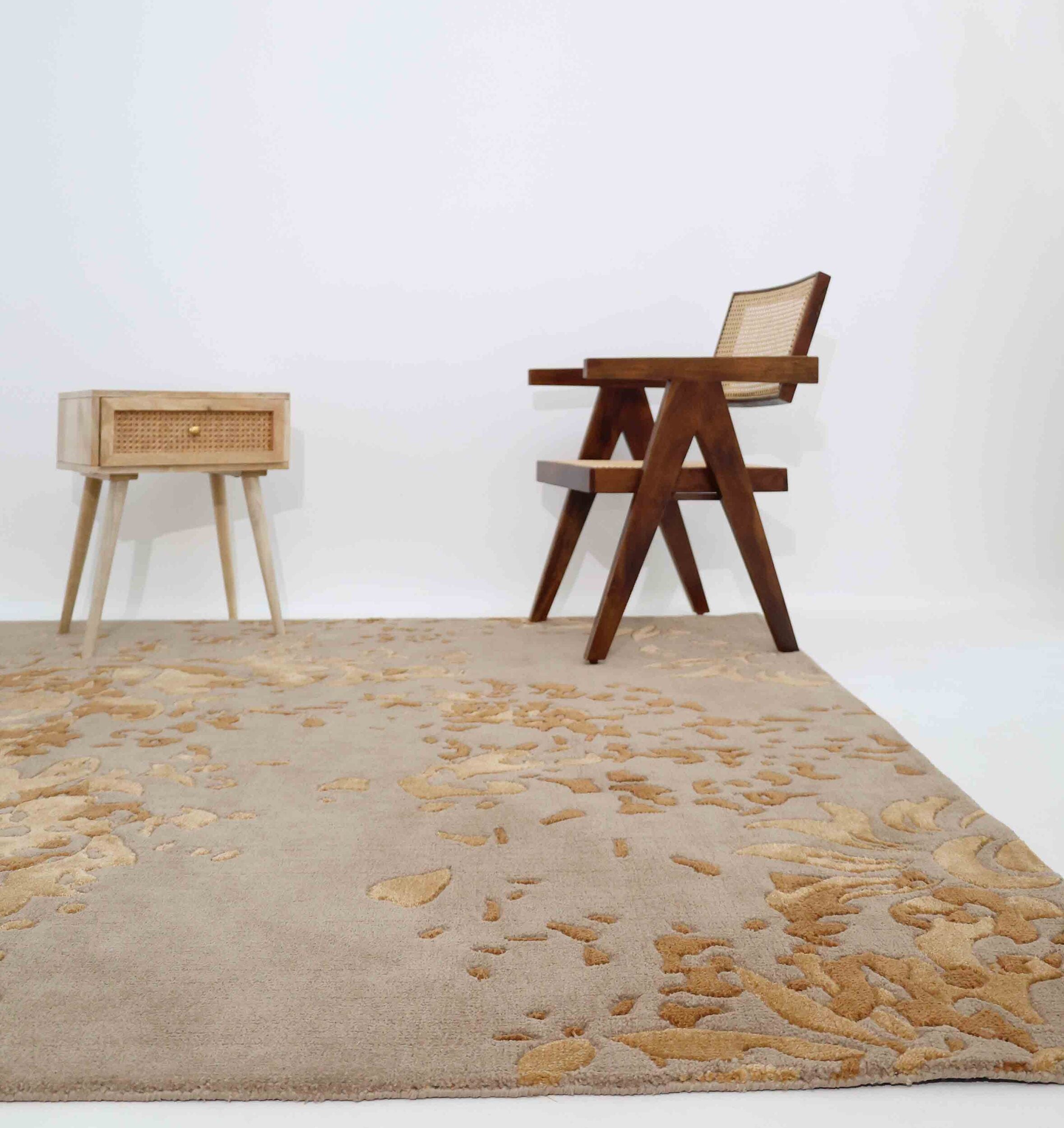 A minimalist room featuring the RAMSHA HOME Luxurious Rectangle Multi Color Novara Rug (CMN 21, 200x300cm), a small wooden table with rattan accents, and a modern wooden chair with woven backrest—all set against crisp white walls.