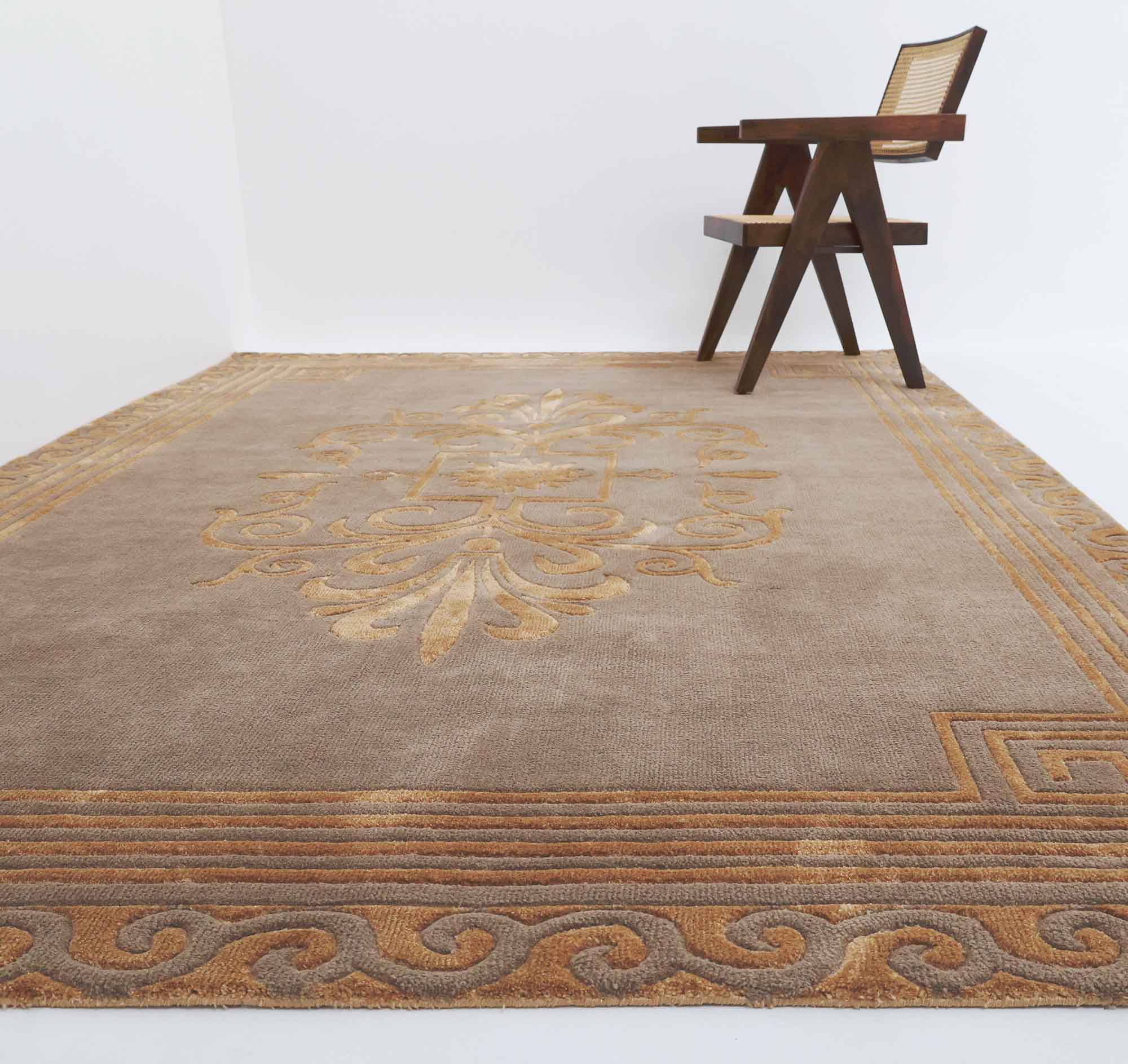 The RAMSHA HOME Beige Rectangle Novara Rugs- CMN 22 (200x300cm) adds elegance to a minimalist room, featuring an ornate central medallion and neutral border, paired with a modern wooden chair against a white wall.