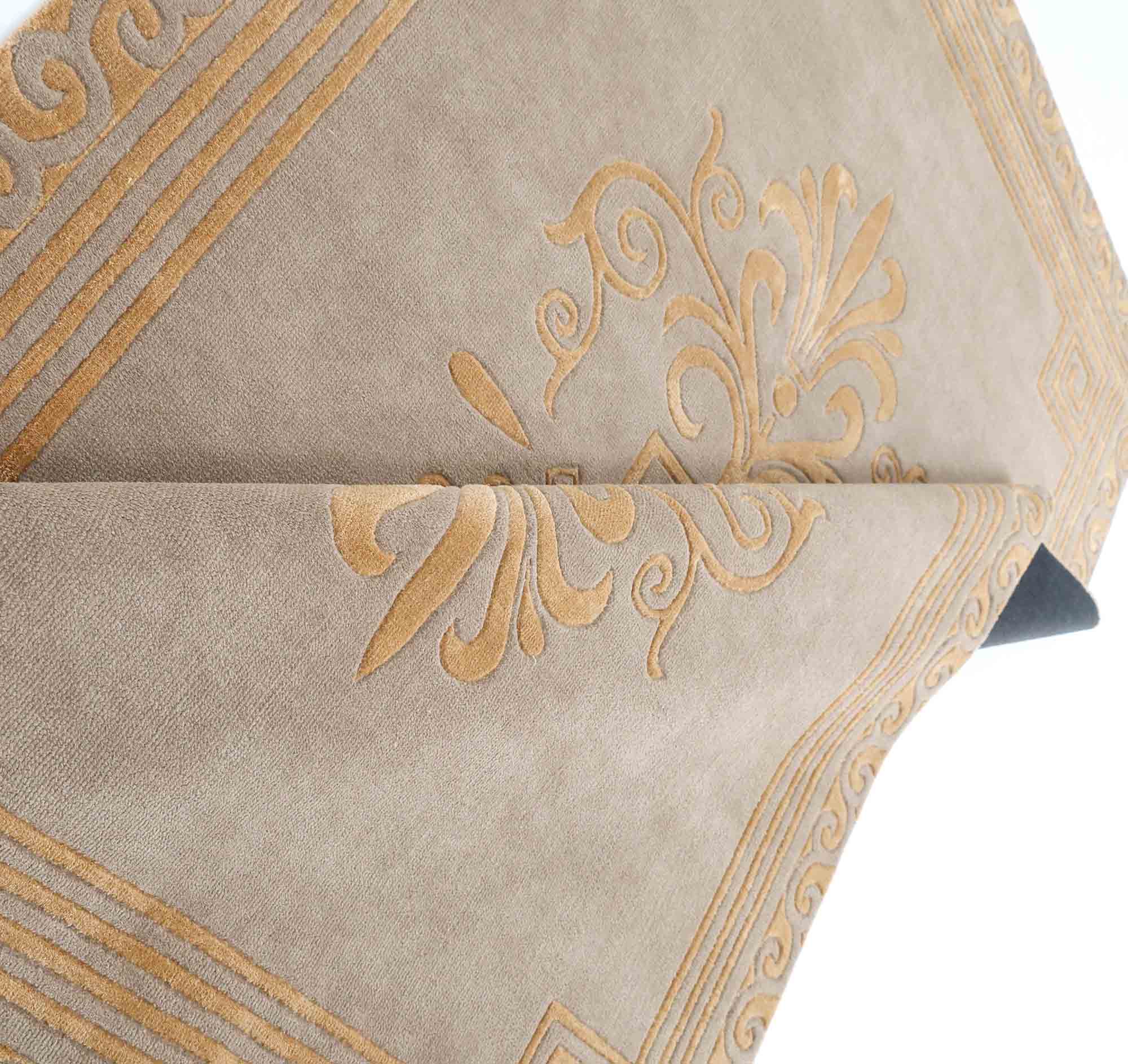 A close-up view of the RAMSHA HOME Beige Rectangle Novara Rugs-CMN 22 (200x300cm), featuring gold embroidered patterns and borders on beige fabric, folded neatly.