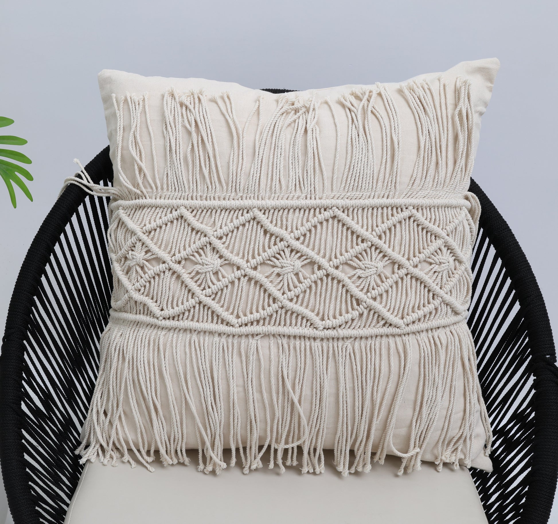 The Ramsha Home Natural Color Jute Cushion with Filler (45x45cm, CS 307) sits on a black woven chair against a plain light background, with a green leaf partially visible on the left.