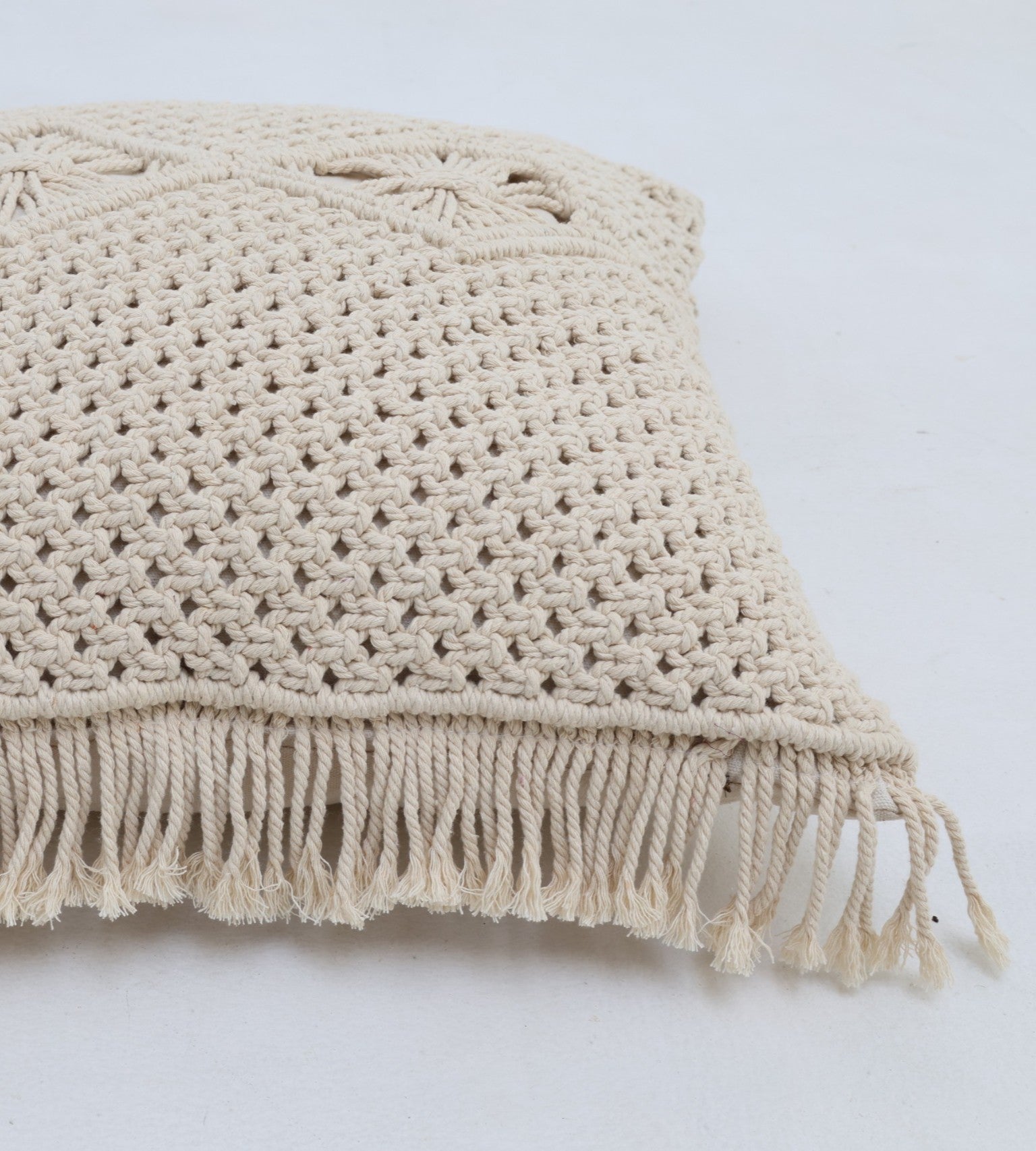 A close-up of the Natural White Macrame Cushion - CS 311 by Ramsha Home, featuring a textured handcrafted pattern and fringed tassels along the edge, displayed on a white surface.