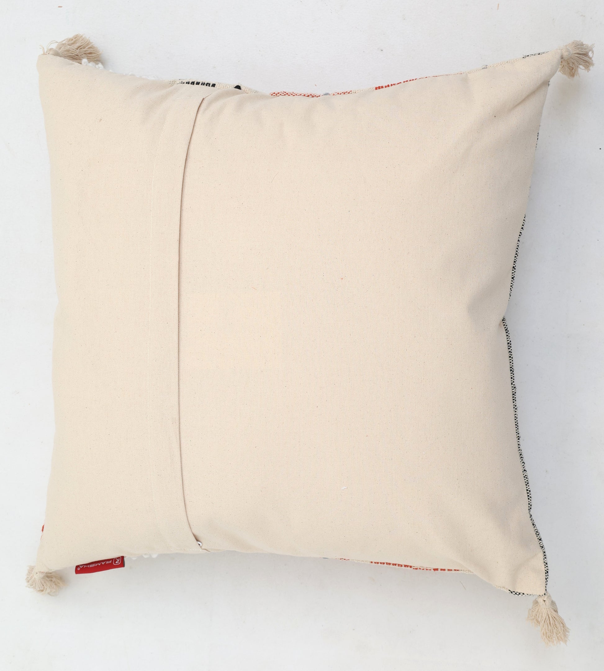 The Cream Color Home Decor Cushion - CS 314 A by Ramsha Home features a premium cotton, off-white square design with corner tassels, back flap, and red tag—perfect for elevating your décor. Displayed against a plain white background.