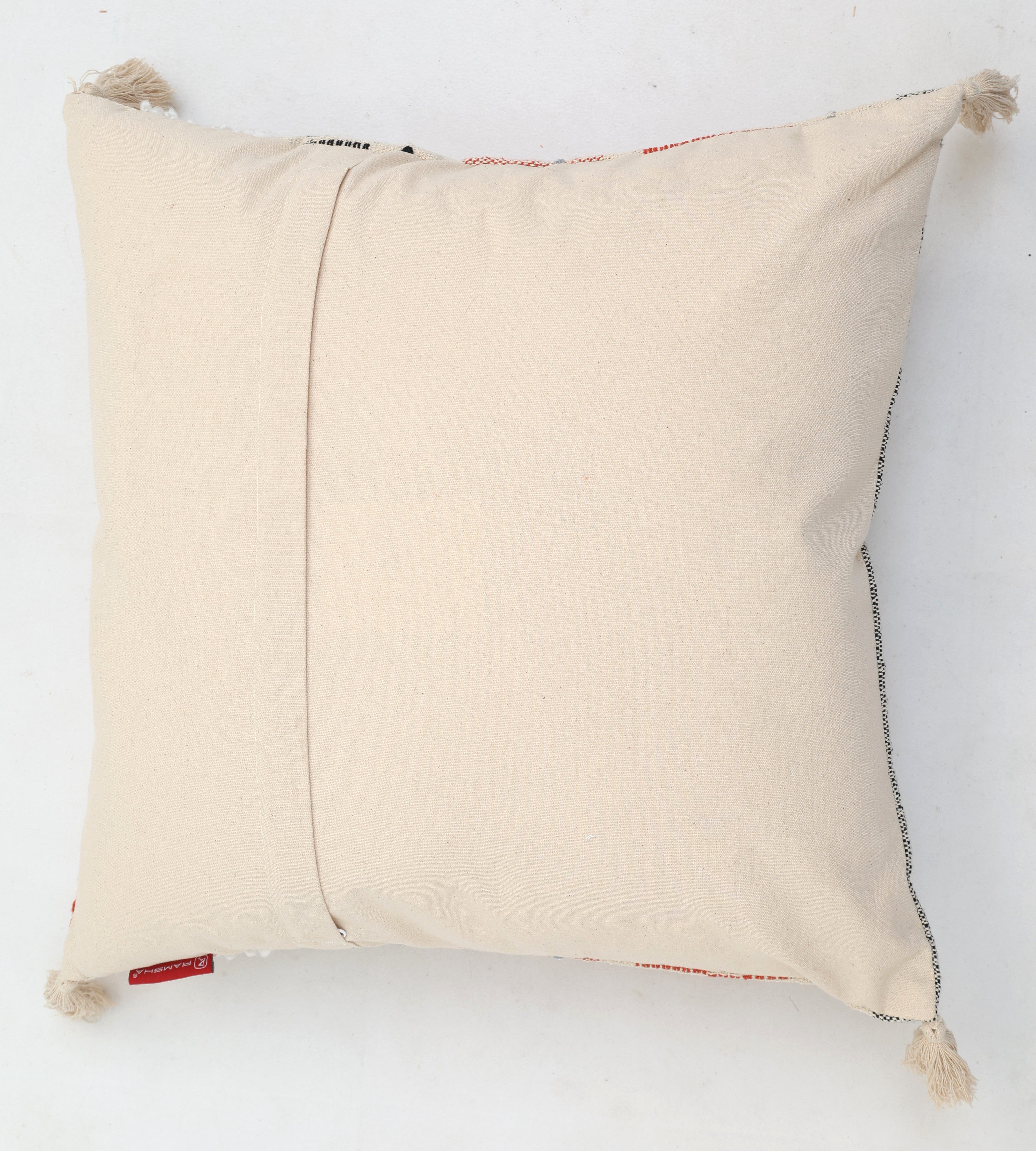 The Cream Color Home Decor Cushion - CS 314 A by Ramsha Home features a premium cotton, off-white square design with corner tassels, back flap, and red tag—perfect for elevating your décor. Displayed against a plain white background.
