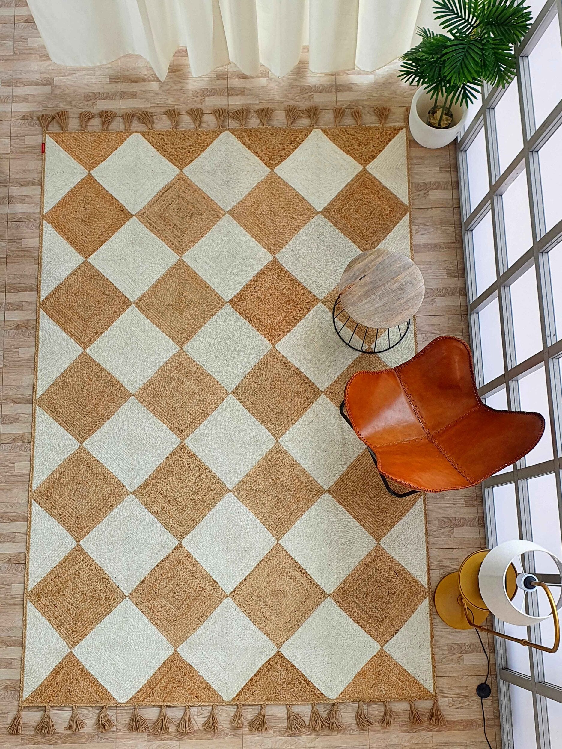 Overhead view of a room featuring the RAMSHA HOME Beautiful Handmade Natural & Bleach Color Jute Braided Rug with Tassel (BR 031), a round wooden side table, brown leather chair, green potted plant, and sunlight through white-curtained windows.